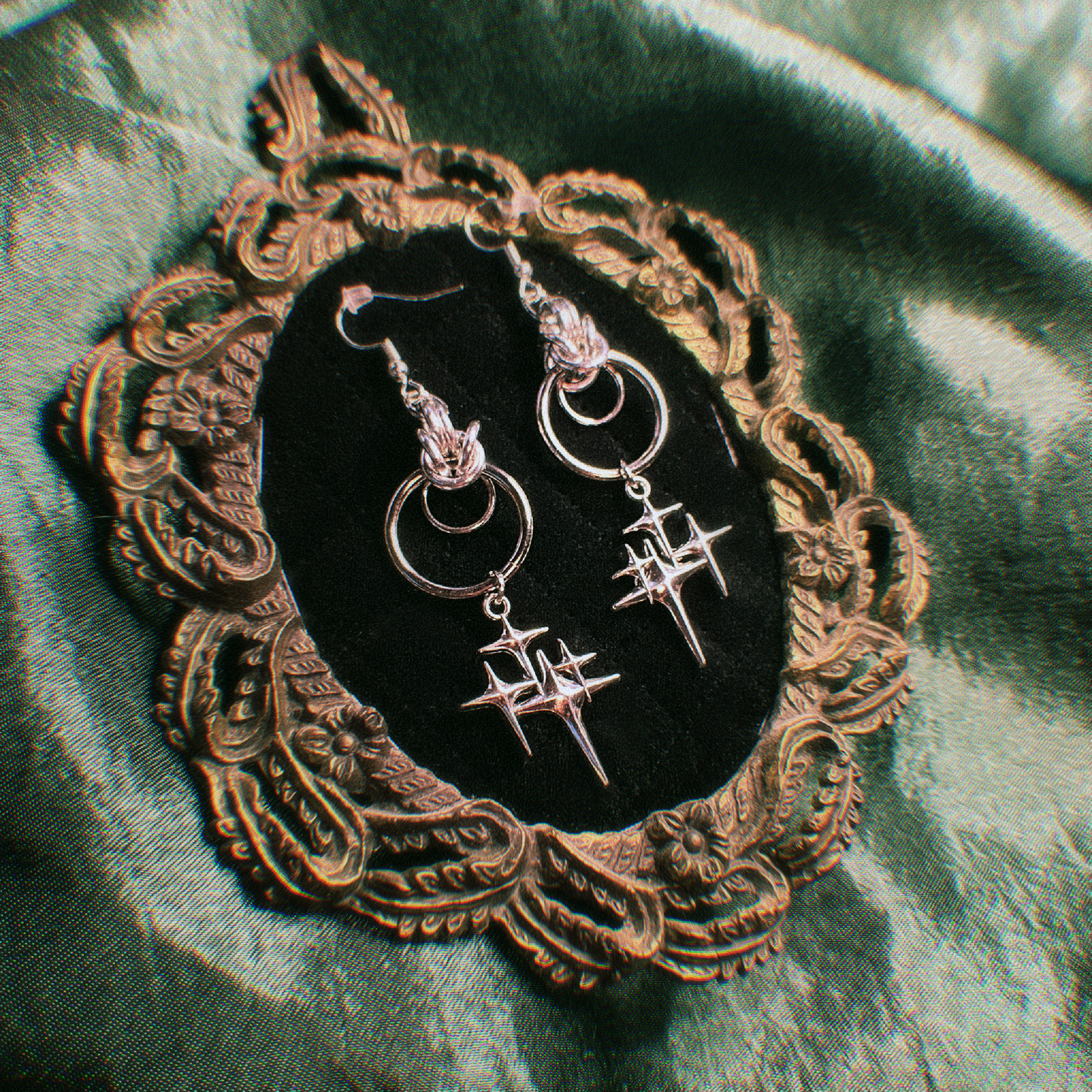Pair of silver earrings on a decorative mirror with a green fabric background