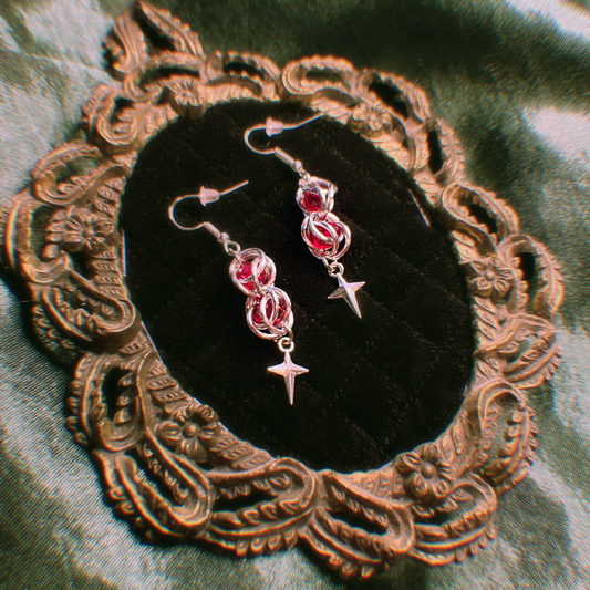 Pair of red and silver earrings on a decorative black velvet pillow with a gold frame.