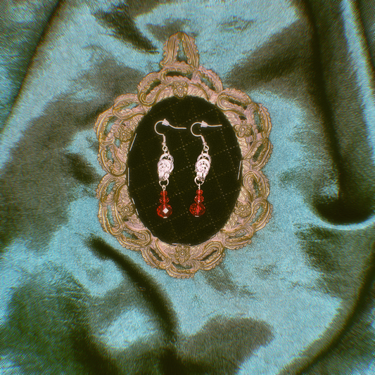 Pair of earrings with red stones displayed in an ornate frame on a green fabric background