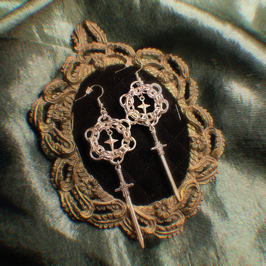 Pair of ornate earrings on a decorative stand with a textured fabric background