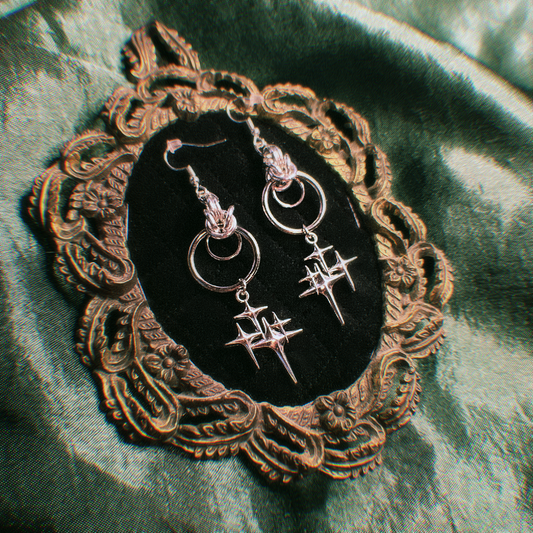 Pair of silver earrings on a decorative mirror with a green fabric background